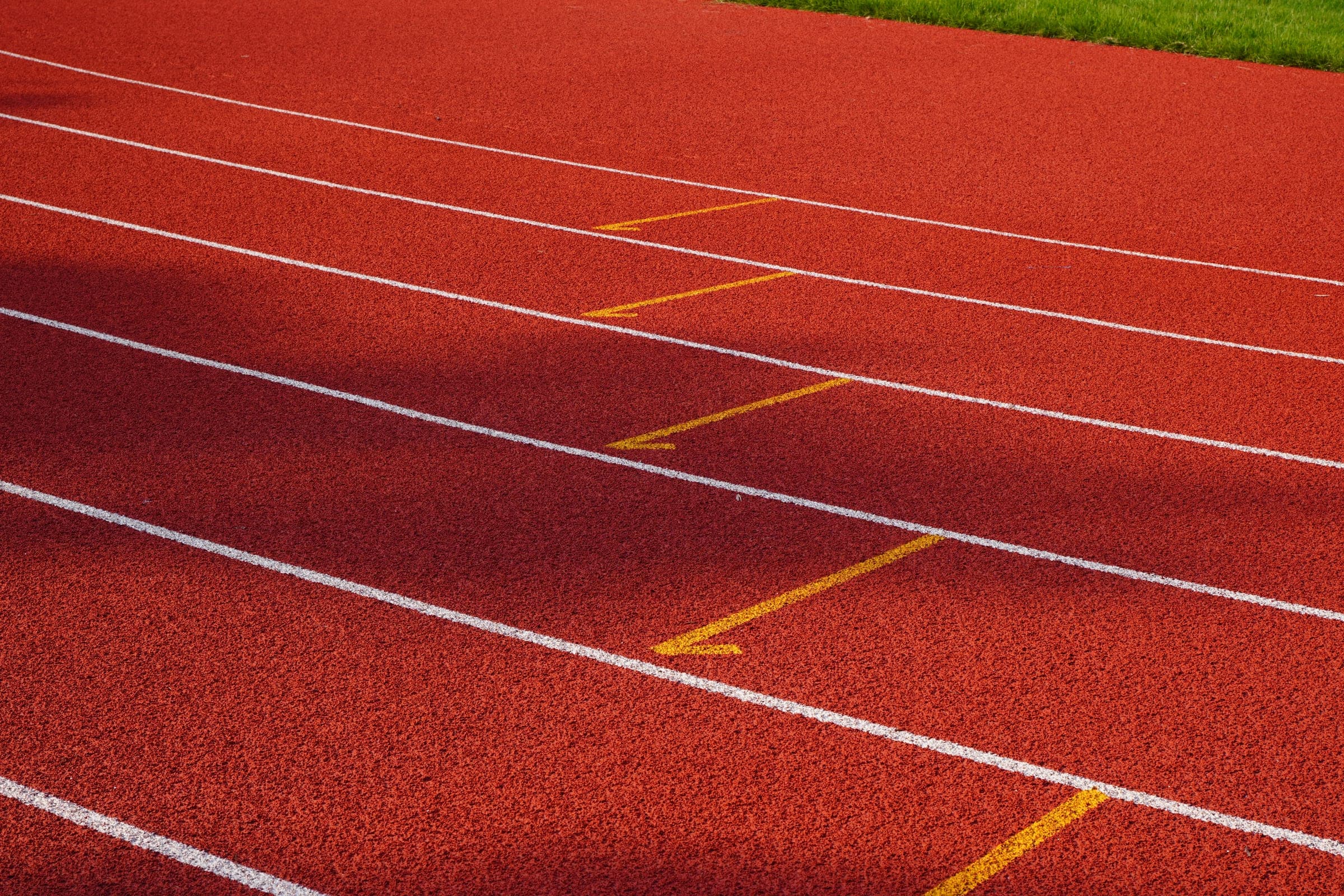 Close-up of the red full-pour track surface across four lanes, white lane lines running diagonally and yellow chevron marks between them.