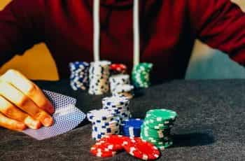 A person sitting in front of several stacks of poker chips while peeking at his cards.