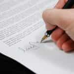 A hand signing a legal document with a pen.