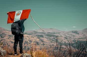 A man carries a Peruvian flag behind his back on a mountain.