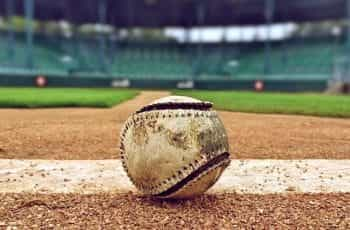 A worn-out baseball sitting in the dirt of a baseball pitch in a baseball stadium before game time.