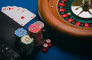 Roulette wheel, casino chips and cards placed next to a laptop.