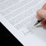 A hand signing a document with a pen.