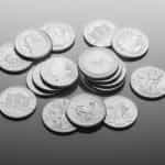 A selection of various silver coins lying flat on a surface, with some facing and showing their heads side, while others face down showing their tails side.