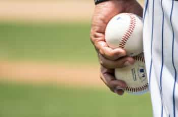 A pitcher during a game of baseball holding two baseballs together in their left hand.